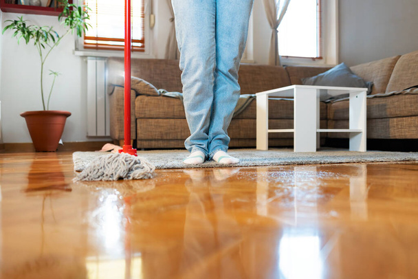 Limpiador sostiene la fregona, primer plano del suelo de parquet y las piernas. Copiar espacio. Servicio de limpieza y tareas. - Foto, imagen