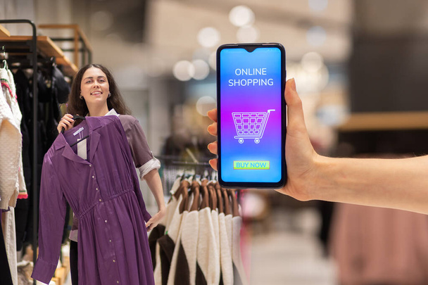 Marketing a reklama. Detailní záběr ženské ruky zobrazující smartphone s nákupy v internetovém obchodě. Hezká žena zkouší nové šaty. Koncept nakupování a slevy. - Fotografie, Obrázek