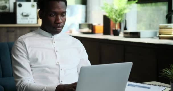 Een serieuze Afro-Amerikaanse man is volledig gefocust als hij werkt op laptop in het thuiskantoor. Zijn toewijding aan zijn taken is duidelijk in deze scène van toegewijde productiviteit. - Video