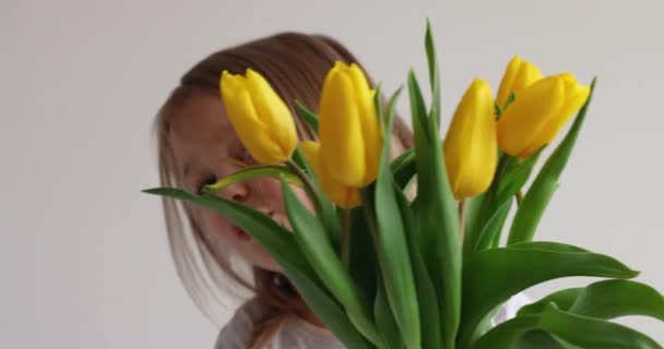 La bambina gioisce e abbraccia in mano un mazzo di tulipani gialli. Concetto per la Festa della Donna, l'inizio della primavera. - Filmati, video