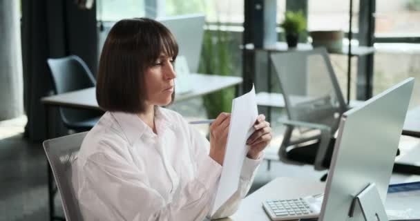 A női irodai dolgozó hatékonyan kezeli a papírmunkát egy professzionális irodai környezetben. Az aprólékos hozzáállása a feladatokhoz azt tükrözi, hogy elkötelezett a szervezettség fenntartása iránt.. - Felvétel, videó