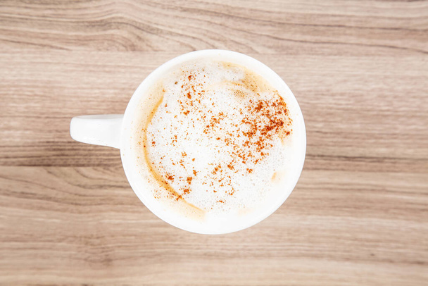 Latte in a white mug with cinnamon sprinkle on a wooden cutting board top down view - Photo, Image