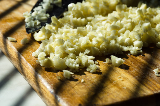 Chopped garlic on a wooden cutting board in a home kitchen. Chopped garlic in the rays of sunlight. - Photo, Image
