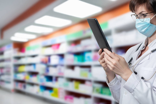 Un farmacéutico mira una tableta contra el fondo de una farmacia. - Foto, imagen