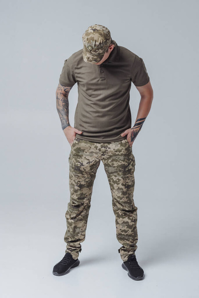 Portret odważnego ukraińskiego wojskowego na sztandarze Ukrainy, koncepcja wolności. Młody człowiek z tatuażami na białym tle - Zdjęcie, obraz
