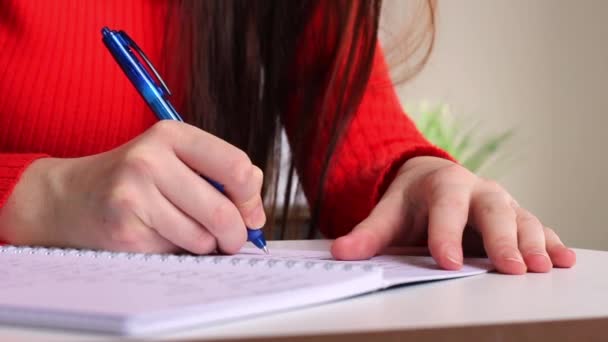 Uma garota na mesa escreve com uma caneta em um caderno. Estudante a estudar, a tomar notas. Escola e educação. Closeup vídeo motion footage - Filmagem, Vídeo