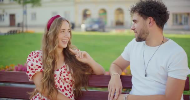 Sorridente giovane donna bionda che parla con il fidanzato mentre si siede sulla panchina in giardino - Filmati, video