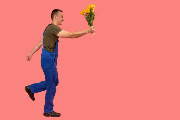 Dostawca w pośpiechu dostarczania kwiatów odizolowanych na różowym tle. Pełnowymiarowy portret kuriera z bukietem. Widok z boku. Przestrzeń kopiowania, makieta - Zdjęcie, obraz