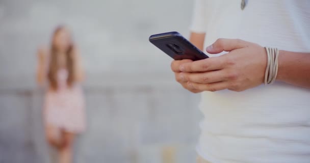 Midsection de mensajería de texto del hombre en el teléfono inteligente con la mujer en segundo plano - Metraje, vídeo