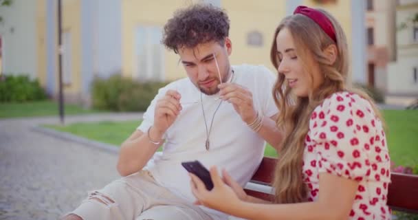 Giovane uomo che indossa occhiali da sole mentre l'amico femminile condivide il telefono cellulare con lui nel parco - Filmati, video