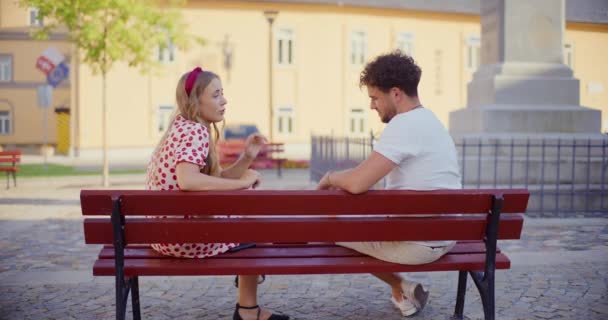 Widok z boku kobieta śpiewa piosenkę siedzi z przyjacielem na ławce w ogrodzie - Materiał filmowy, wideo