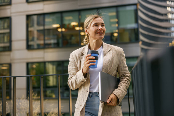 Женщина-менеджер собирается на работу, выпивая кофе на фоне офисного здания. Высокое качество фото - Фото, изображение