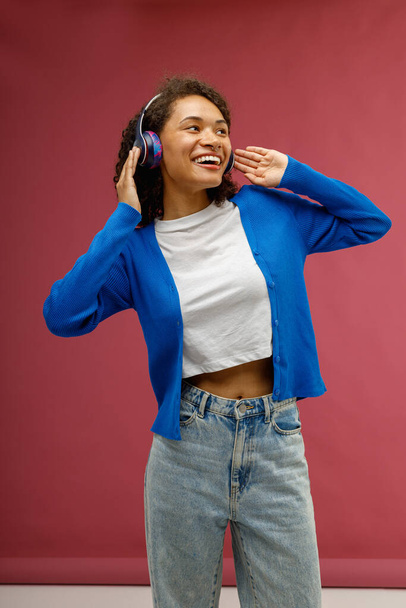 Smiling woman enjoy music touching headphones standing on red studio background. High quality photo - Photo, Image