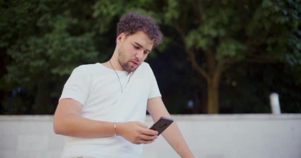Przystojny młody człowiek SMS-y na smartfonie w ogrodzie - Materiał filmowy, wideo