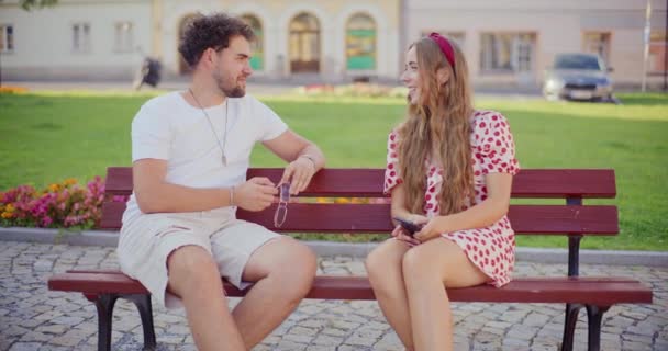 Felice donna bionda che parla con il fidanzato mentre si siede sulla panchina in giardino - Filmati, video