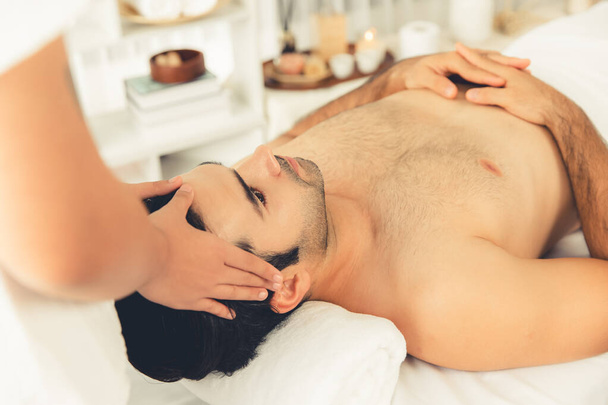 Caucasian man enjoying relaxing anti-stress head massage and pampering facial beauty skin recreation leisure in dayspa modern light ambient at luxury resort or hotel spa salon. Quiescent - Photo, Image