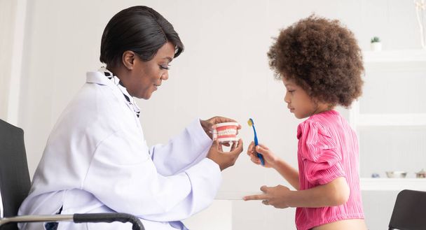 African American dentist explaining to mixed-race afro child how to brush teeth. The doctor and healthcare concept for children. - Photo, Image