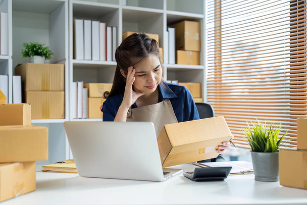 Jonge vrouw online ondernemer stress probleem over het voorbereiden van een pakket doos om het pakket voor te bereiden voor levering aan de klant. - Foto, afbeelding