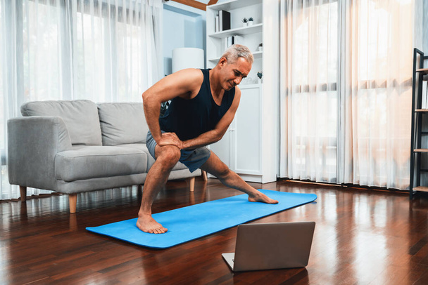 Aktif ve formda bir adam, evde egzersiz yapmadan önce ısınma ve esneme hareketleri yapıyor ve çevrimiçi fitness videosu izliyor. Emekliler için sağlıklı yaşam tarzı konsepti. Etki - Fotoğraf, Görsel
