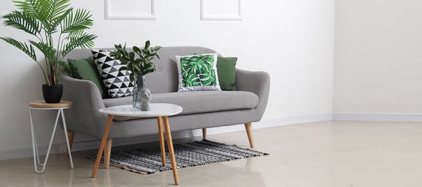 Accogliente divano grigio con cuscini e piante d'appartamento su tavoli vicino alla parete bianca - Foto, immagini