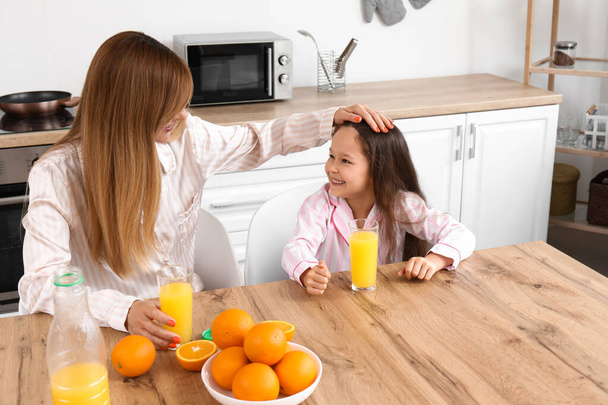 Niña con su madre bebiendo jugo de naranja en casa por la mañana - Foto, imagen