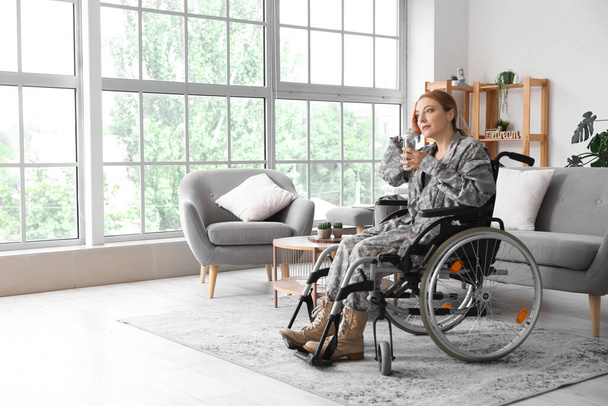Female soldier in wheelchair with glass of water at home - Foto, afbeelding