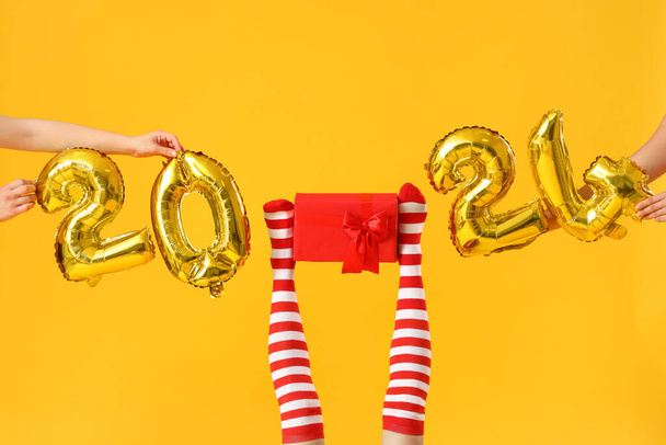 Mujer joven en medias de Navidad con figura 2024 sobre fondo amarillo - Foto, Imagen