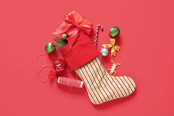 Kerstsok met mooie decoraties en geschenkdoos op rode achtergrond - Foto, afbeelding