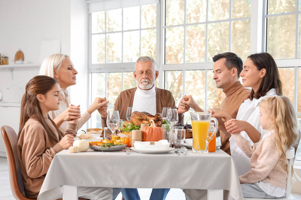 Szczęśliwa rodzina modli się przed kolacją przy świątecznym stole w Święto Dziękczynienia - Zdjęcie, obraz