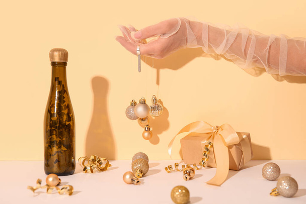 Noel kompozisyonu, kadın eli mücevher, bir şişe şampanya ve sarı arka planda beyaz masada hediye paketi. - Fotoğraf, Görsel