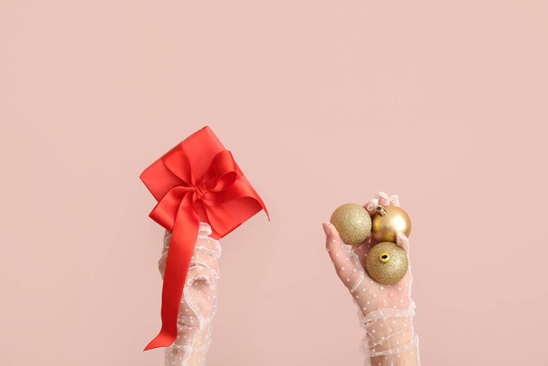 Female hands holding Christmas baubles and red gift box on pink background - Photo, Image
