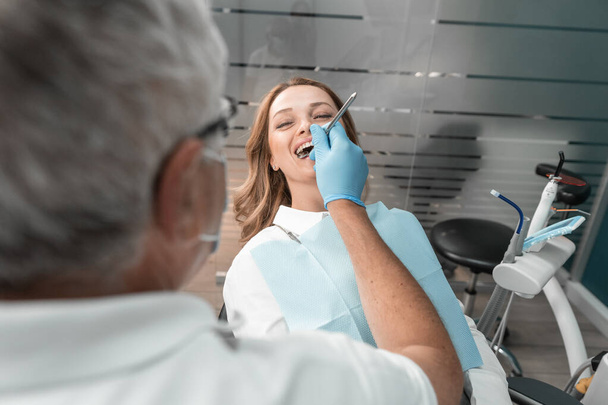 Ο ασθενής αισθάνεται επαγγελματική φροντίδα και εμπιστοσύνη στον οδοντίατρο κατά τη διάρκεια της επίσκεψης στην κλινική. Μια γυναίκα σε ραντεβού με οδοντιάτρους. Οι πλέον σύγχρονες μέθοδοι και εξοπλισμός εξασφαλίζουν υψηλό επίπεδο οδοντιατρικής περίθαλψης. - Φωτογραφία, εικόνα