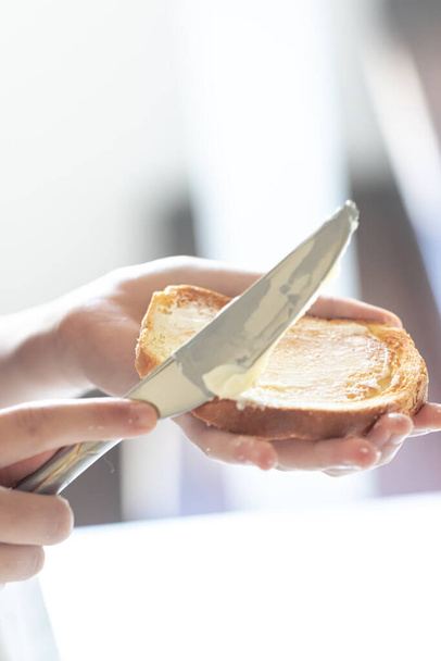 Un pedazo de pan con mantequilla en la mano de una mujer, concepto de desayuno saludable. - Foto, Imagen