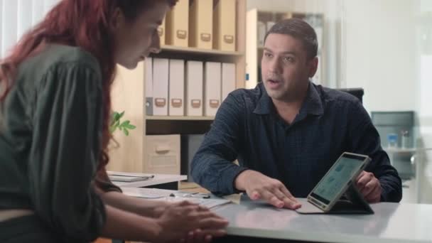 Mediana toma de empresario mostrando nueva estrategia de empresa en tableta digital a comercializador durante reunión en oficina - Metraje, vídeo