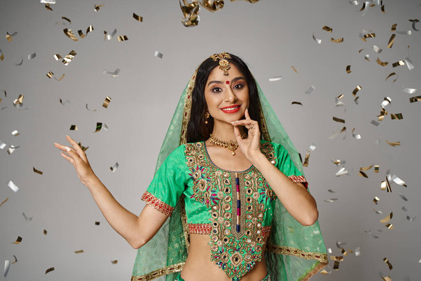 vidám fiatal indiai nő nemzeti ruhák bindi és zöld fátyol körül konfetti - Fotó, kép