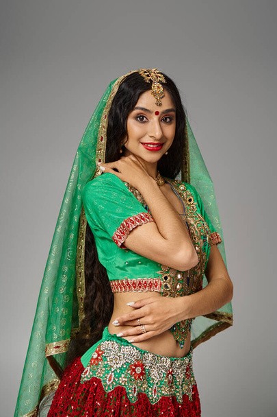 tiro vertical de la atractiva mujer india con el pelo largo y bindi punto sonriendo alegremente a la cámara - Foto, Imagen