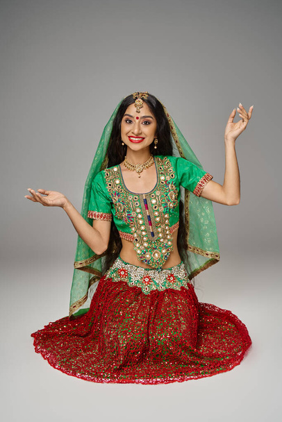 alegre joven india mujer en falda roja y verde choli gesto y sonriendo felizmente a la cámara - Foto, imagen