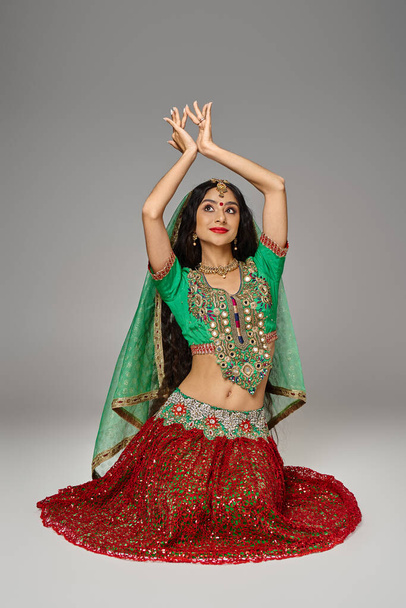 dobře vypadající mladá indiánka v tradičním oblečení sedí na podlaze a gestikuluje pažemi - Fotografie, Obrázek