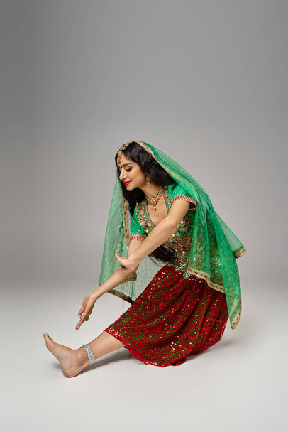 グレーの背景で踊っている間,ビンディドットジェスチャーと全国コスチュームの魅力的なインドの女性 - 写真・画像