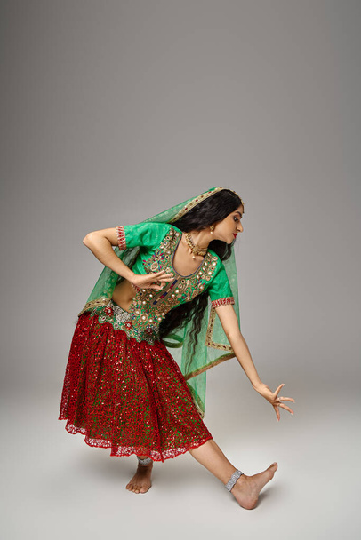 tiro vertical de la atractiva mujer india en choli verde y falda roja gestos mientras baila animado - Foto, imagen