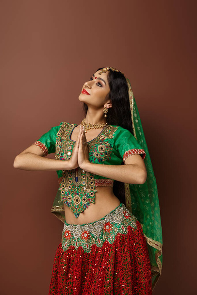 вертикальный снимок индийской женщины с бинди и зеленой вуалью, показывающей молитвенный жест и отводящей взгляд - Фото, изображение