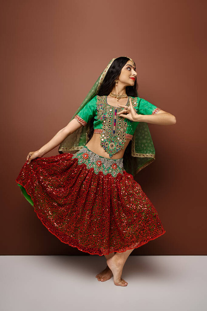krásná indická žena v tradičním oděvu se závojem a bindštinou aktivně tančící a odvracející pohled - Fotografie, Obrázek