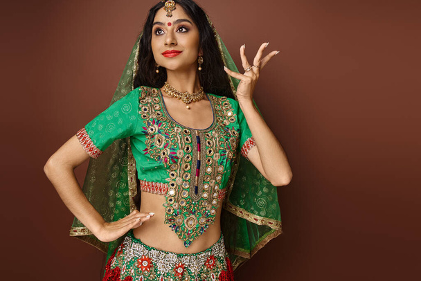 attraktives indisches Model in grünem Choli mit Bindi Dot gestikulierend beim Tanzen, wegschauend - Foto, Bild