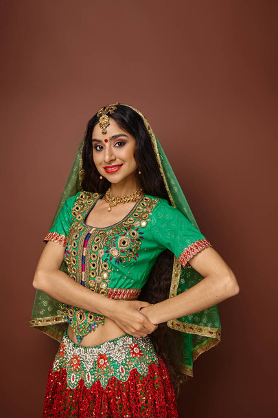 tiro vertical de mulher indiana bonita com cabelos longos e véu verde sorrindo alegremente para a câmera - Foto, Imagem