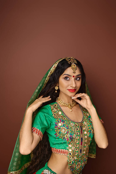 pionowy strzał atrakcyjnej hinduskiej kobiety w zielonej, tradycyjnej choli z bindi i akcesoriami - Zdjęcie, obraz