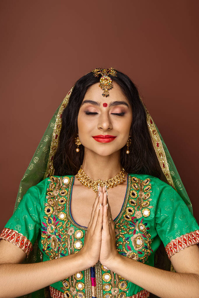 vertical shot of beautiful indian woman in national clothes showing praying gesture with closed eyes - Photo, Image