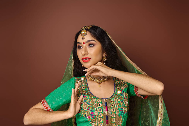 hermosa mujer india joven en traje tradicional con accesorios gestos y mirando hacia otro lado - Foto, Imagen