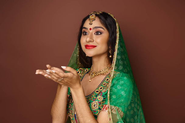 gyönyörű fiatal indiai nő hagyományos ruhákban pózol nyitott tenyérrel és félrenéz - Fotó, kép