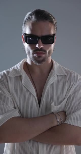 sexy módní muž se slunečními brýlemi skládací paže, dívá se stranou a dopředu a smyslně dotýká rty na šedém pozadí - Záběry, video
