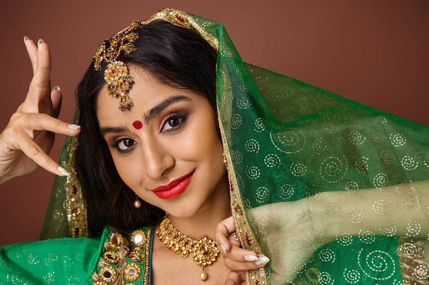 atractiva mujer india alegre con punto bindi y velo verde gestos y mirando a la cámara - Foto, Imagen